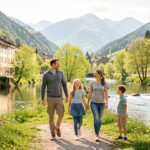 Une famille se promène au bord d’une rivière à Saint-Girons, entourée de verdure, de fleurs printanières et de montagnes pyrénéennes.