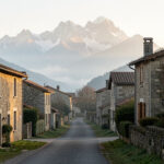Vue éditoriale d’un village pyrénéen de Haute-Garonne au petit matin, avec des maisons de pierre, un sentier balisé et les sommets montagneux en arrière-plan dans une lumière douce.