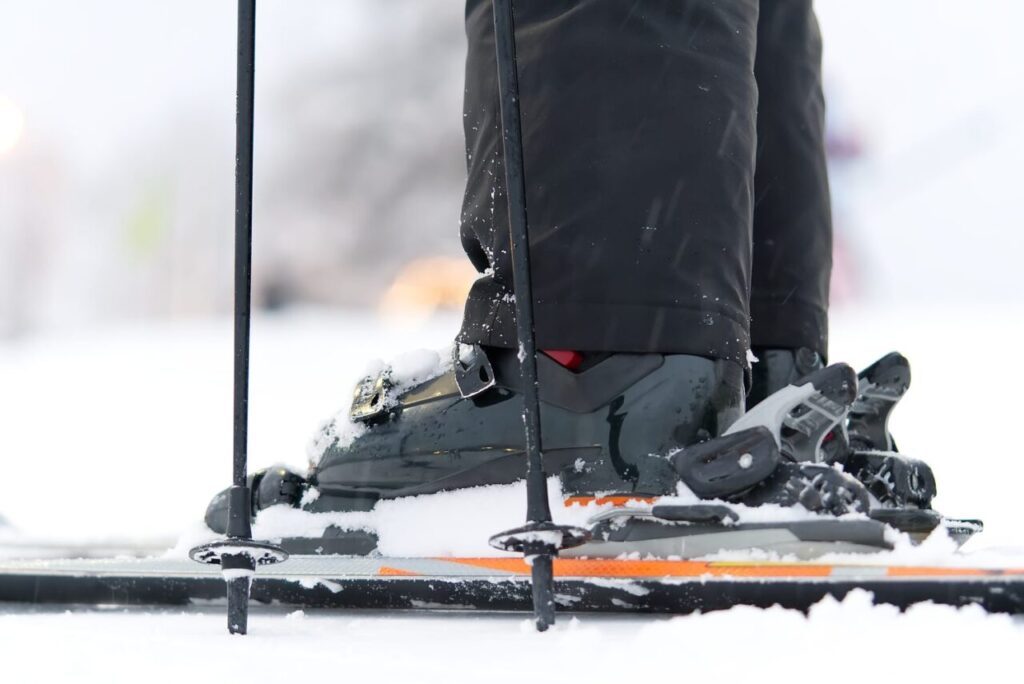 Skieur ajustant ses chaussures de ski avant sa première descente sur une piste enneigée.