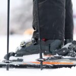 Skieur ajustant ses chaussures de ski avant sa première descente sur une piste enneigée.